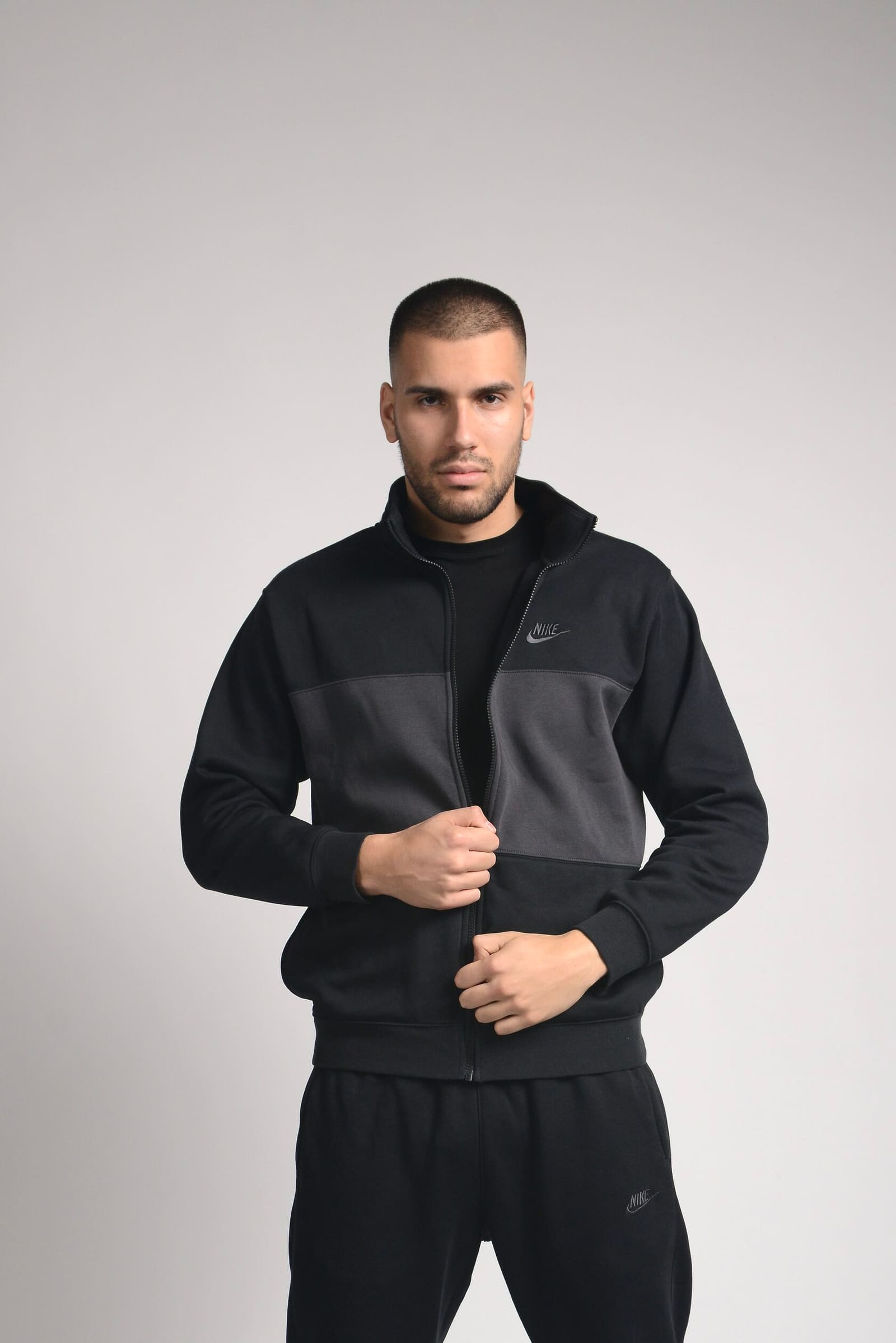 A man in a black and grey tracksuit on a light backdrop, a clothing shot