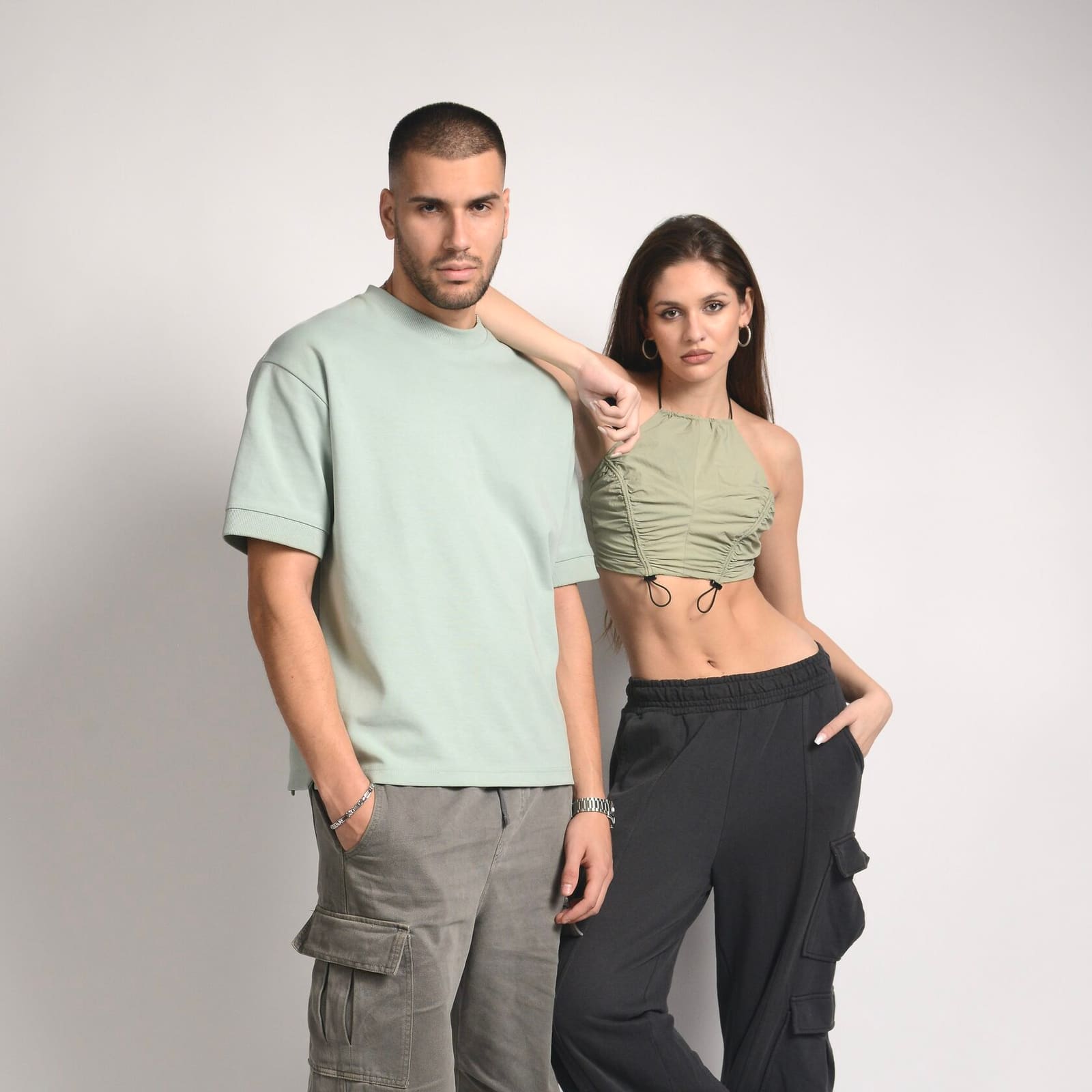 A man in a mint T-shirt and a woman in a crop top and black cargo trousers, a studio clothing shot